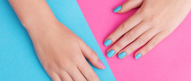 Female hands with pink and blue painted nails against a split pink and blue background.