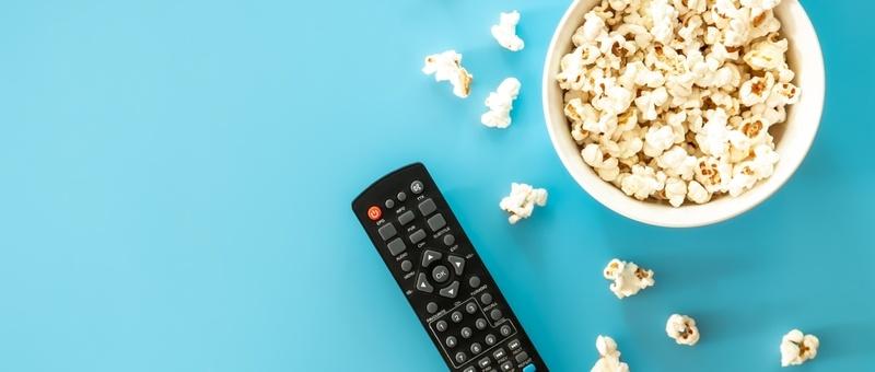 TV remote and popcorn against blue background.