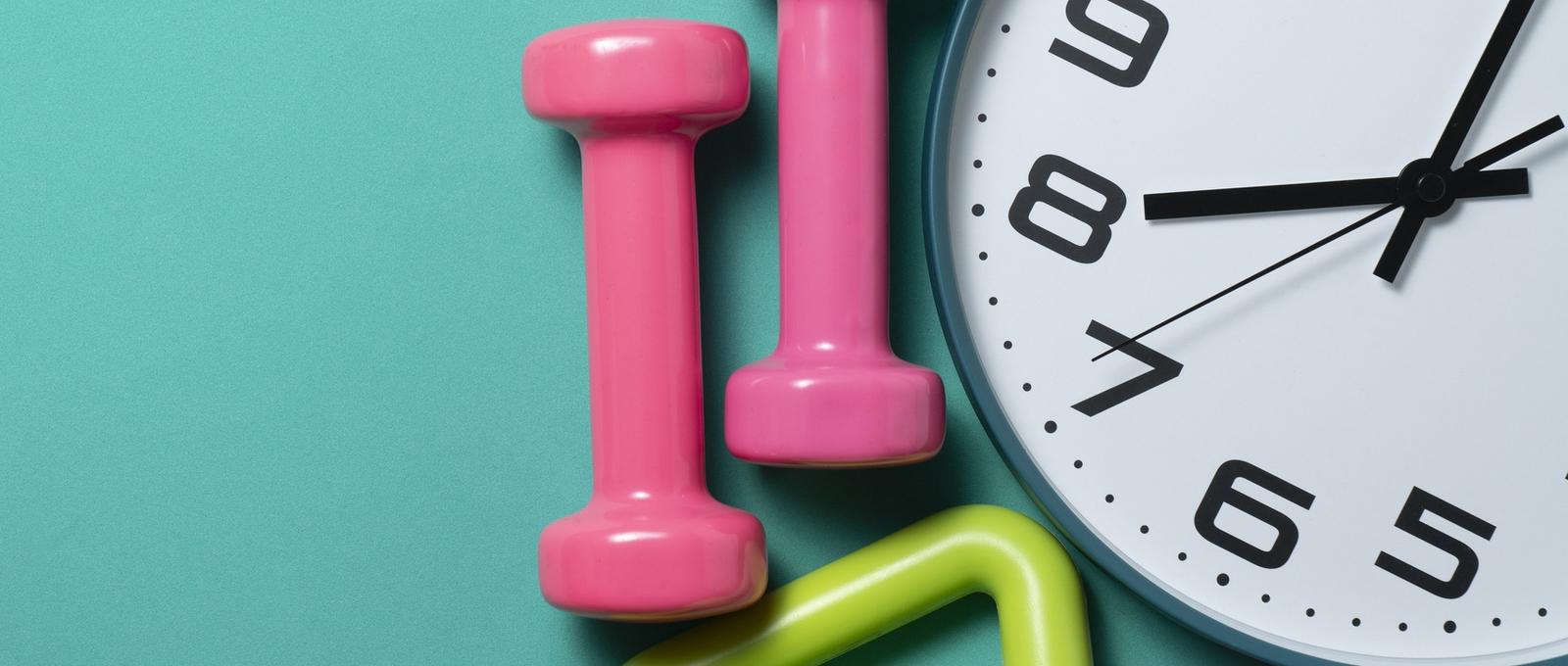 Time for exercising clock and dumbbell with green table background