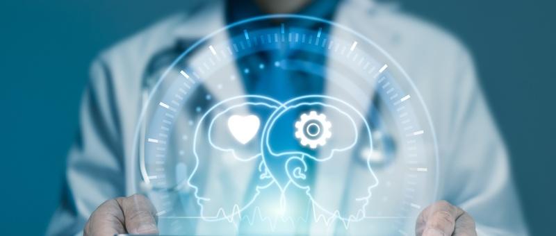 Medical professional holding digital hologram showing two profile heads with heart and gear symbols representing healthcare technology.