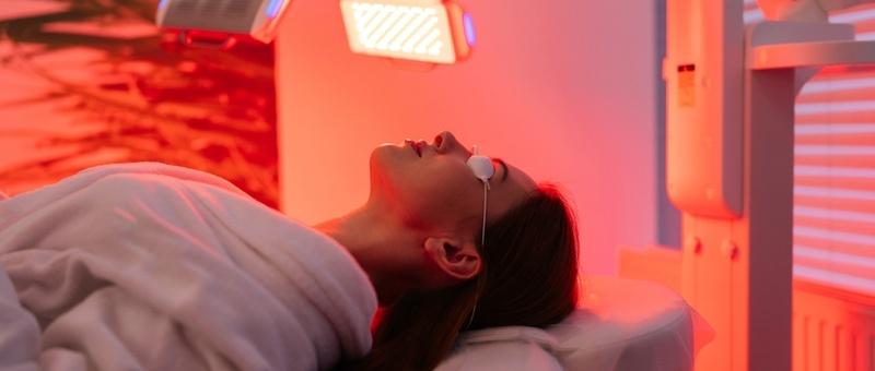 Woman laying down in a spa setting, receiving red light therapy from a machine.