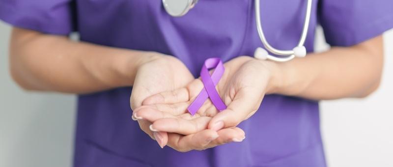 Health professional in purple scrubs holding purple ribbon in both hands.