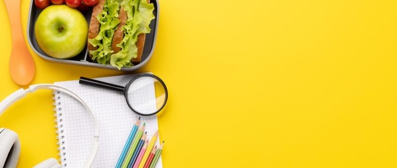 Packed lunch with school study tools against a yellow background.