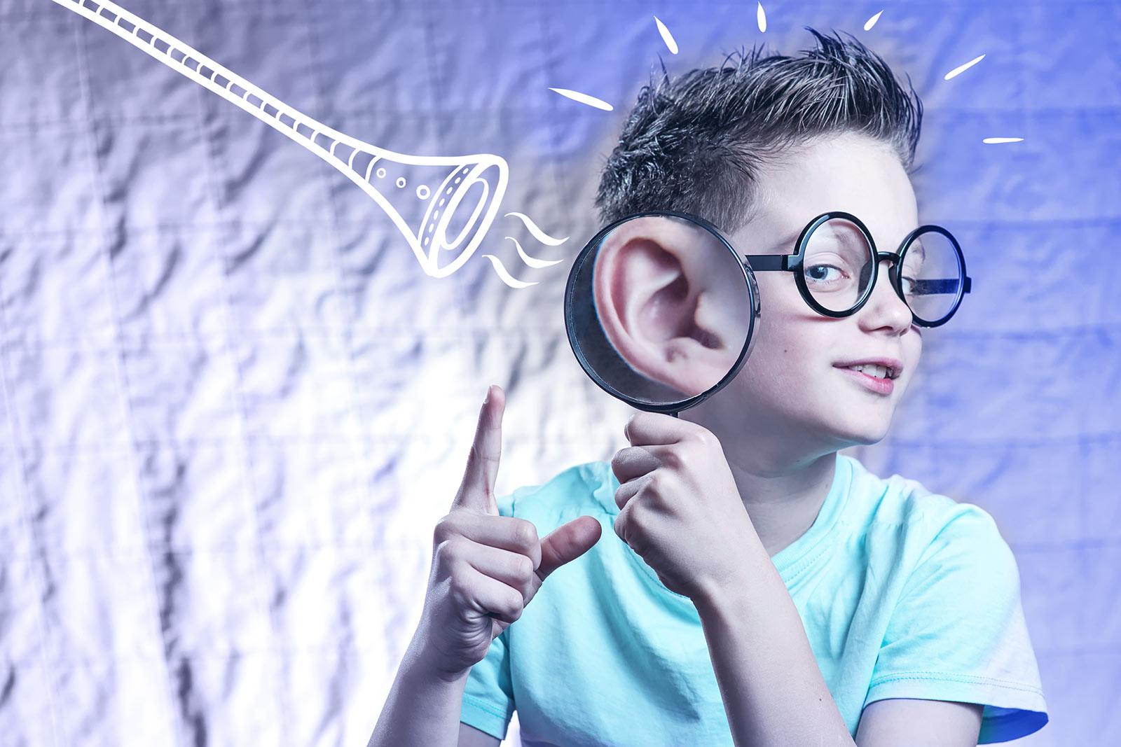 Child wearing round glasses and holding magnifying glass to ear, with illustrated trumpet sound waves nearby.