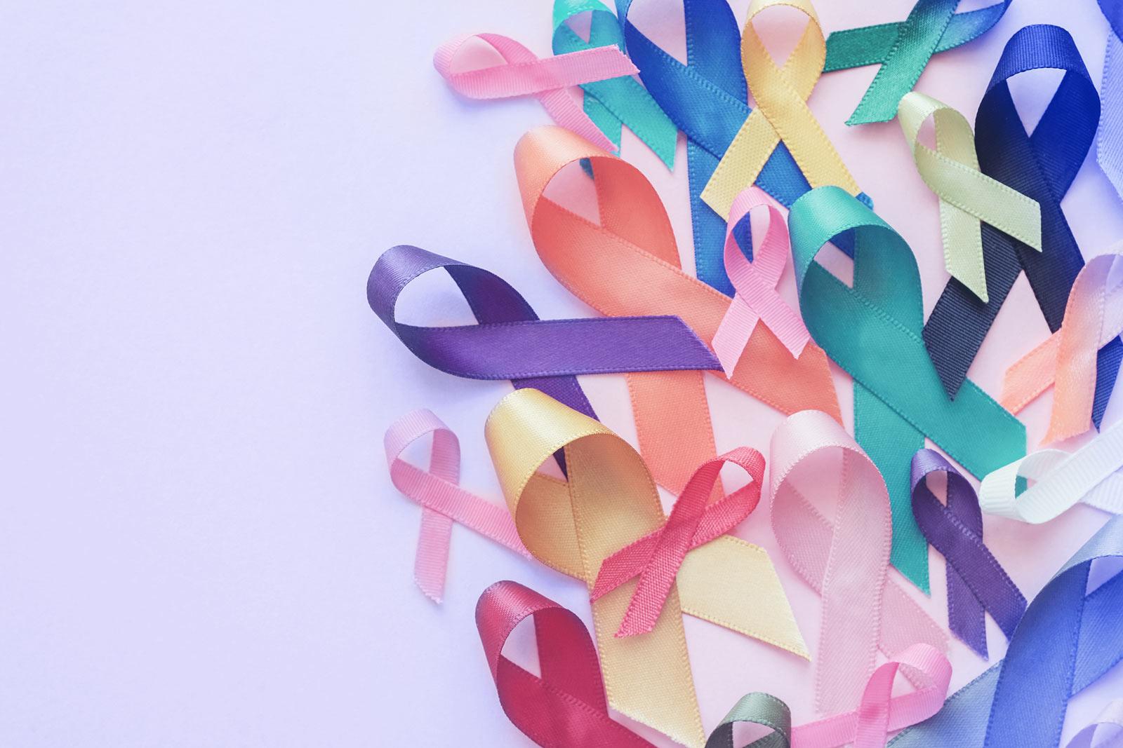 Colourful awareness ribbons in pink, blue, yellow, green, purple and orange scattered on a white background.