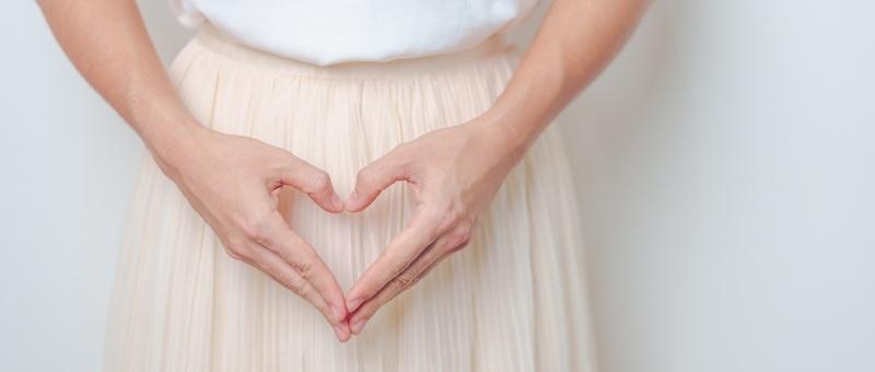 Female figure wearing white top and skirt with hands in heart-shaped position.