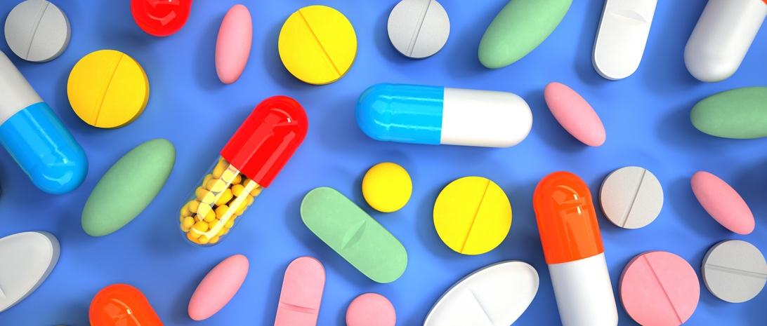 Colourful assortment of pills, tablets and capsules scattered on blue background, including red, yellow, blue and green medications.