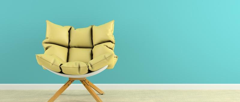 Armless white wooden armchair with yellow cushions against a blue wall background on pale-coloured flooring.
