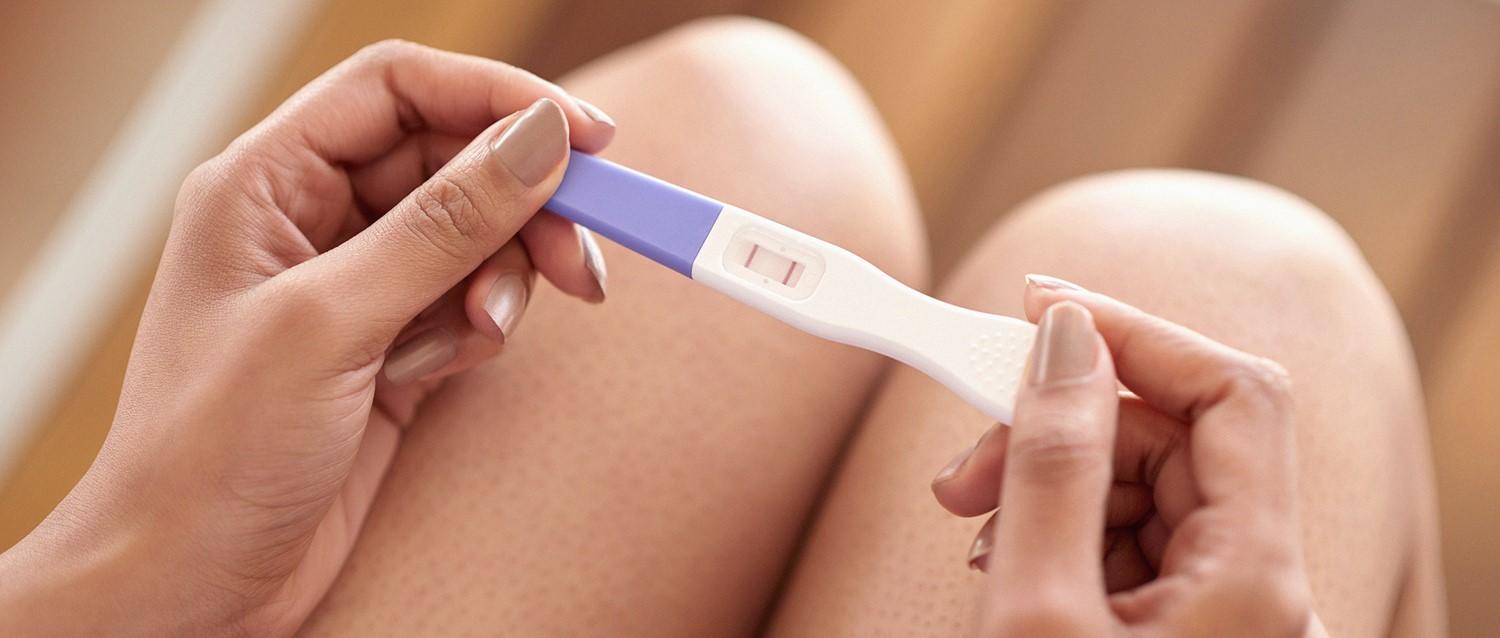 Hands holding a positive pregnancy test against a pregnant belly background.