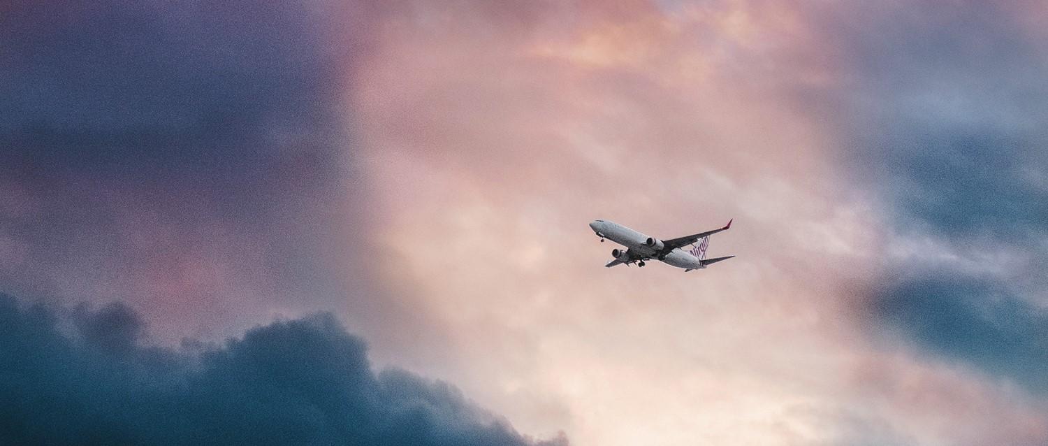 Virgin aircraft flying through dramatic pink and blue cloudy sky at dusk.